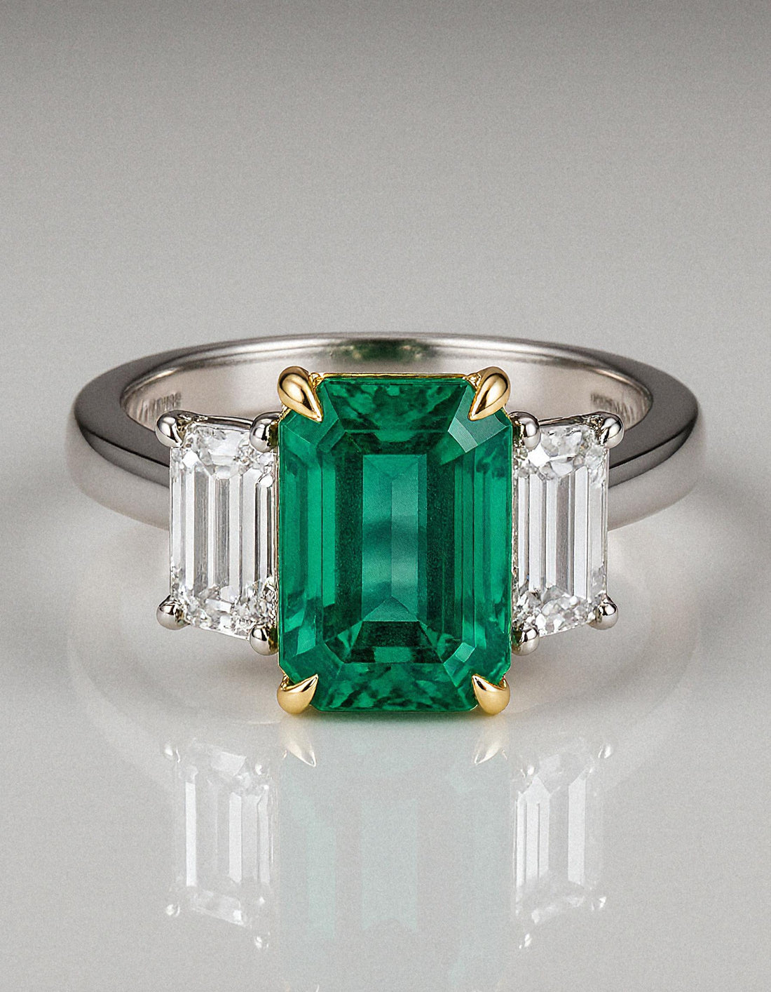 &quot;Abigail&quot; White and yellow gold three-stone ring with an emerald-cut Green emerald center and trapezoid diamond side stones.